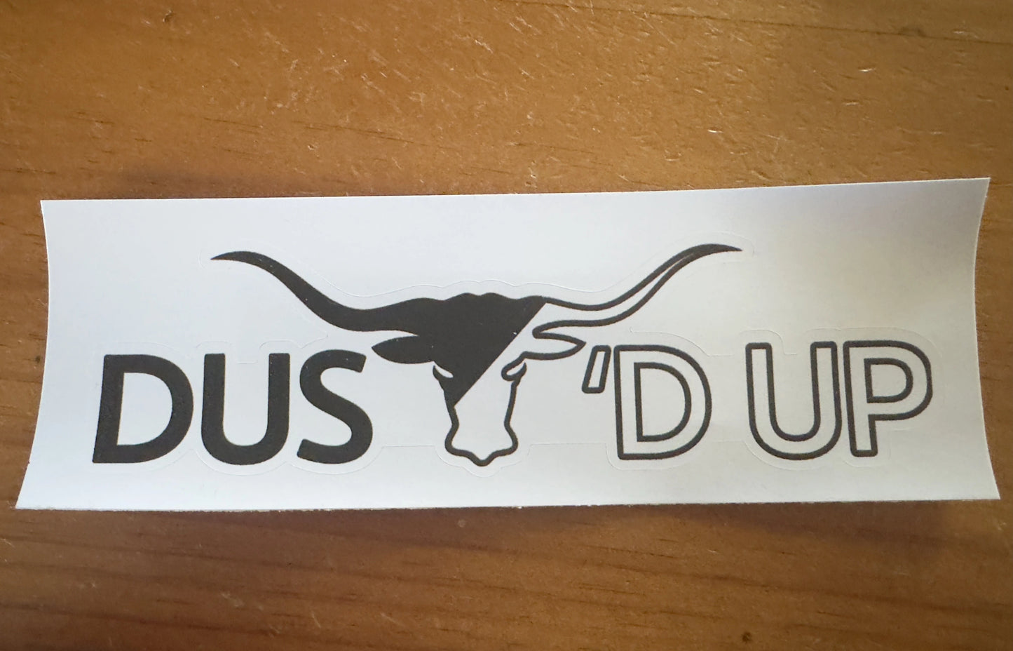 Sticker with 'DUST D'UP' text and a logo on a wooden surface