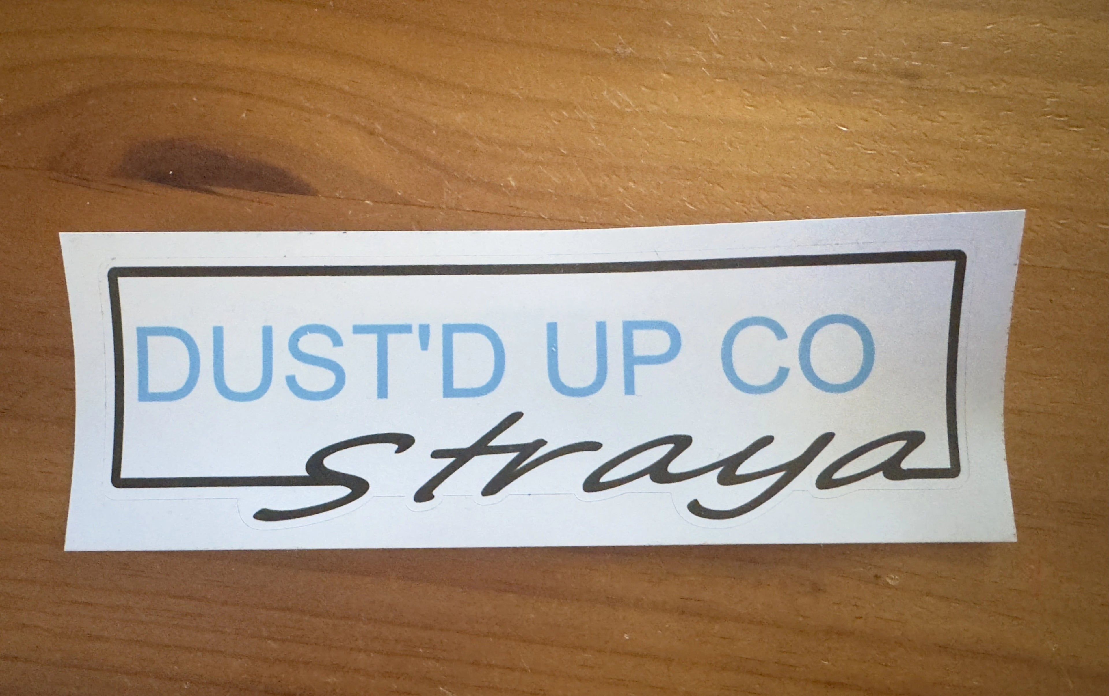 Sticker with 'Dust'd Up Co' text on a wooden surface