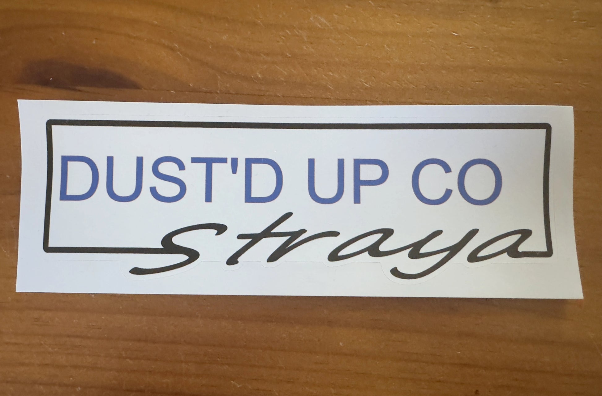 Sticker with 'DUST'D UP CO' text on a wooden surface