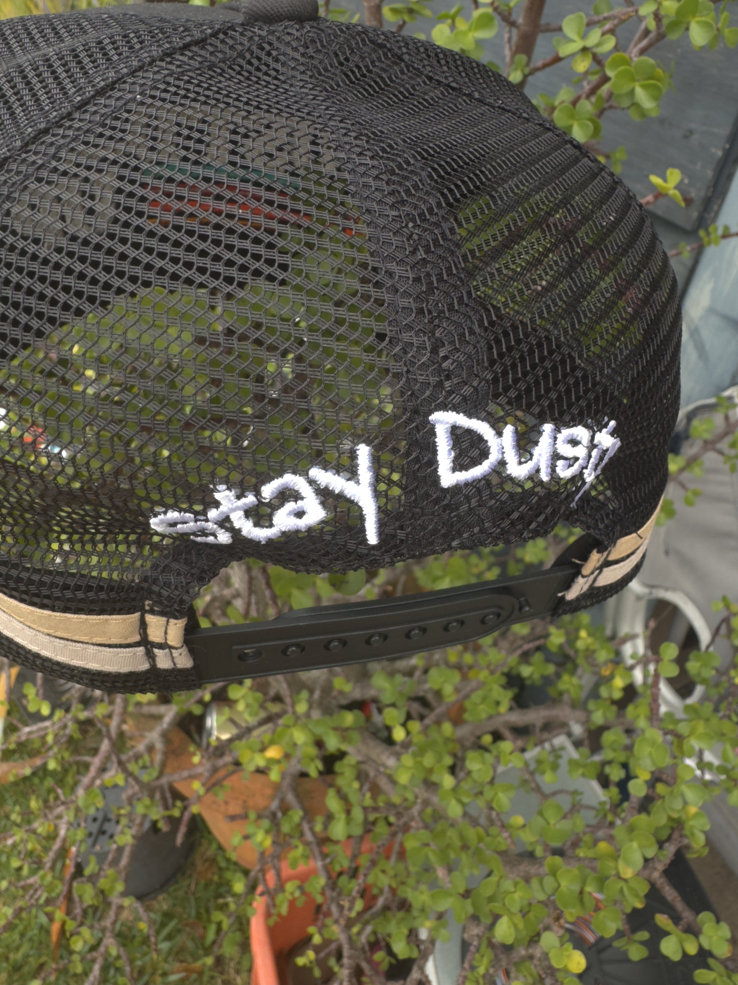 Black mesh cap with 'Stay Dusty' text on a blurred natural background