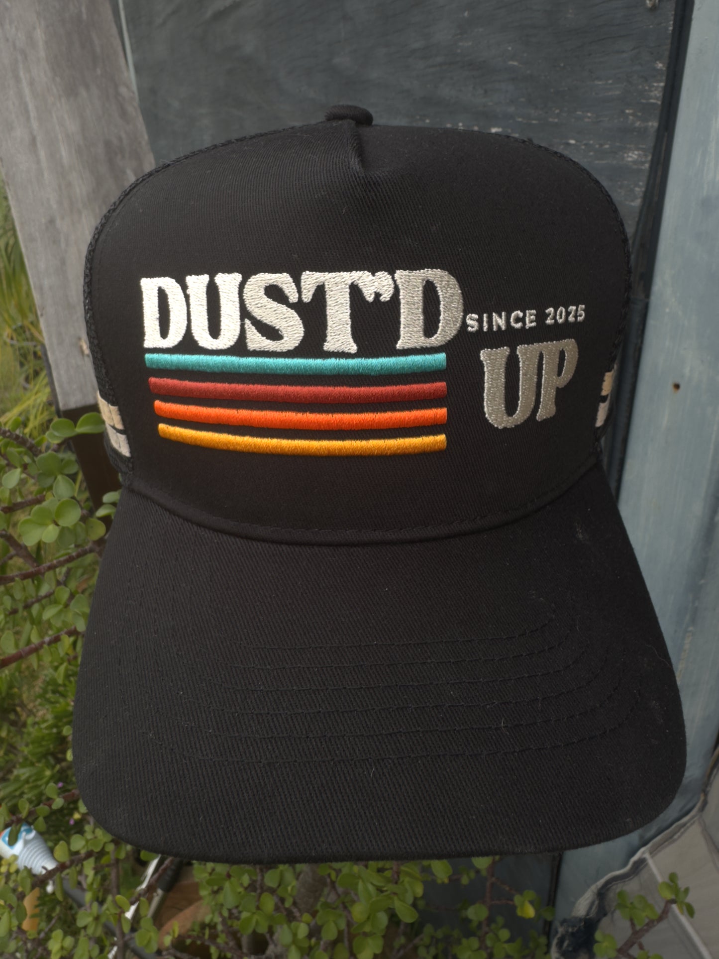 Black cap with 'DUST'D UP' text and colorful stripes on a tent background
