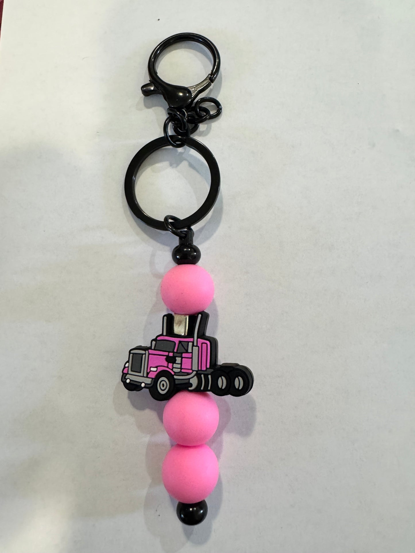 Keychain with pink beads and a black cross charm on a white background