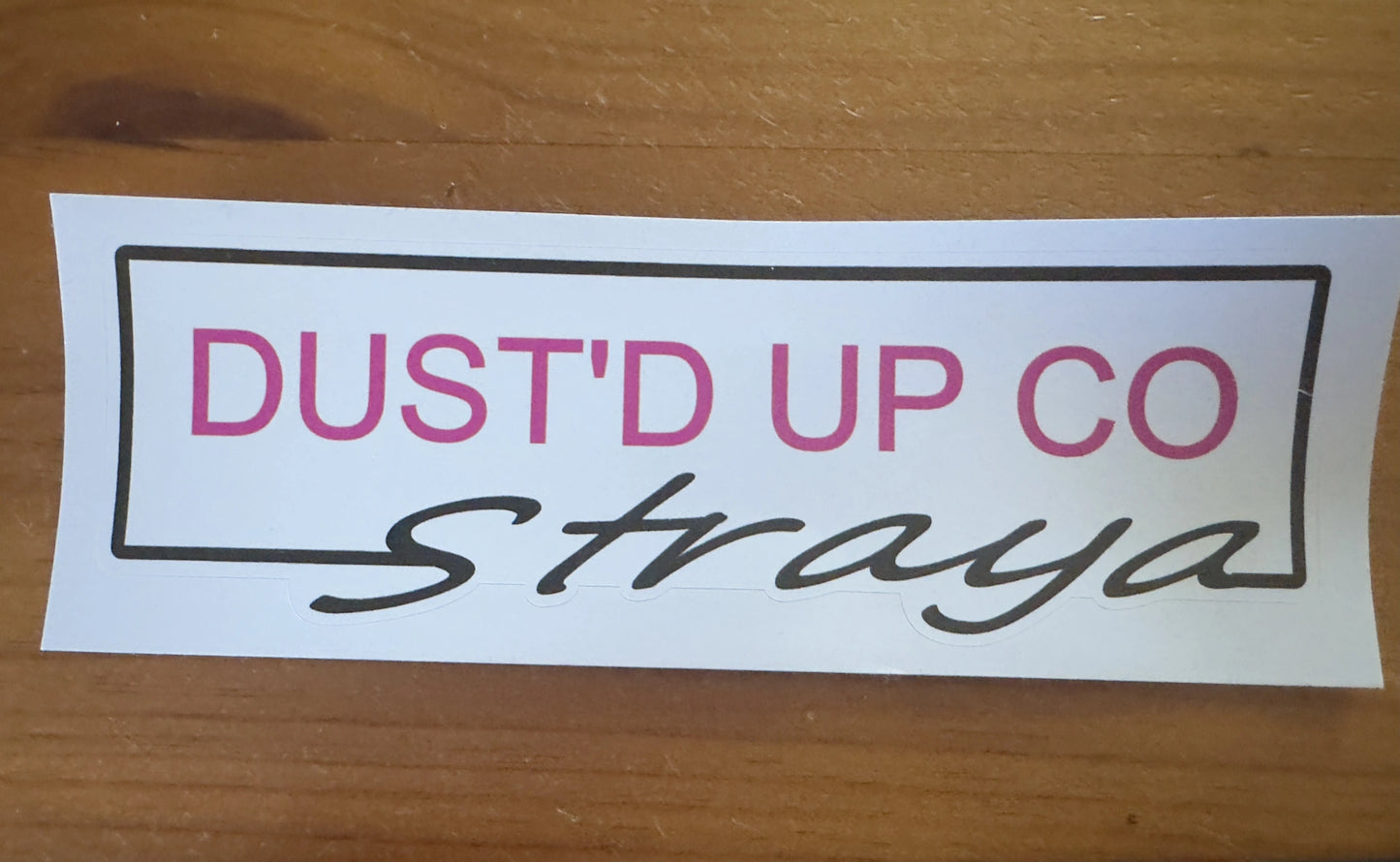 Sticker with 'Dust' Up Co' text on a wooden surface